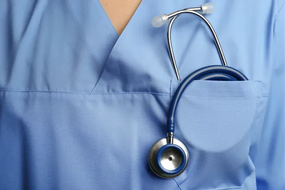 A healthcare professional wearing light blue scrubs with a matching blue stethoscope tucked into the chest pocket.