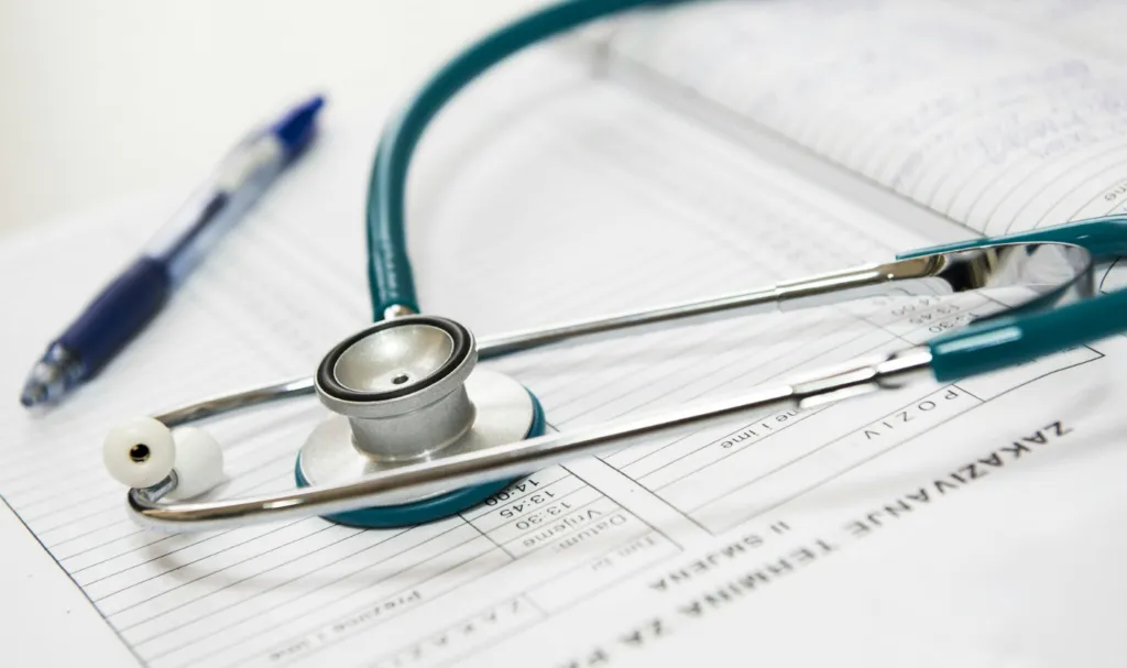 A teal stethoscope resting on a medical document next to a pen.