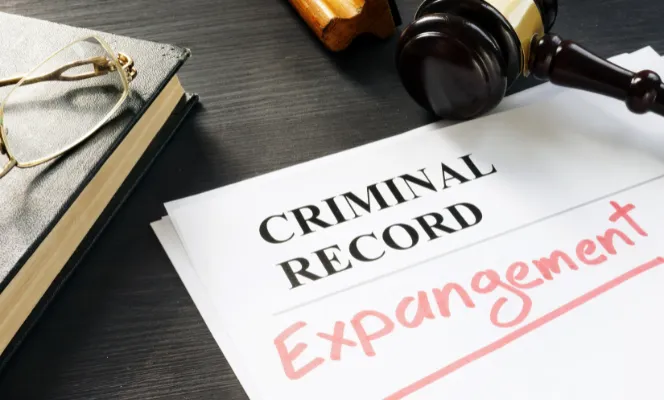 A document titled "Criminal Record Expungement" next to a gavel, glasses, and a book on a dark wooden surface.
