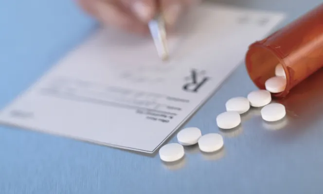 A prescription pad and pills spilling from a medicine bottle.
