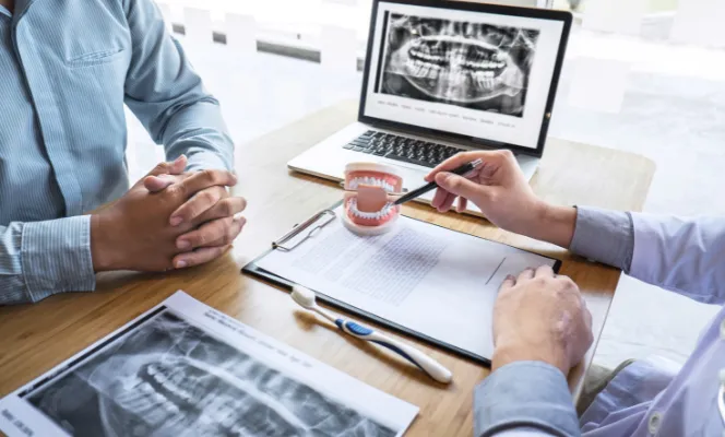 A dentist explaining treatment options to a patient using a dental model and X-rays.