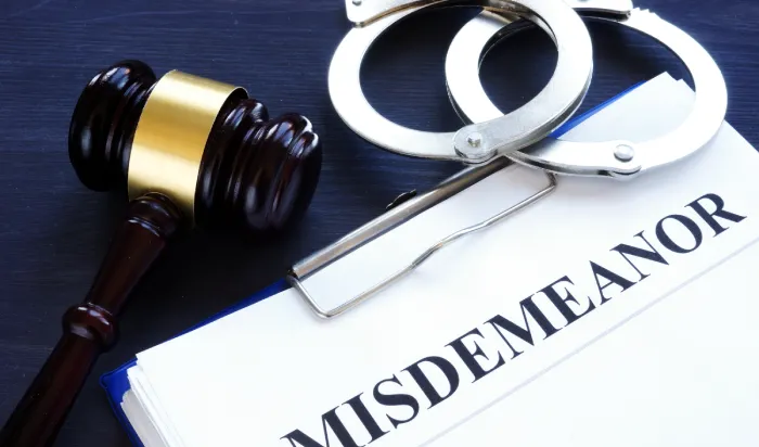 A gavel and handcuffs resting on a document labeled "MISDEMEANOR".
