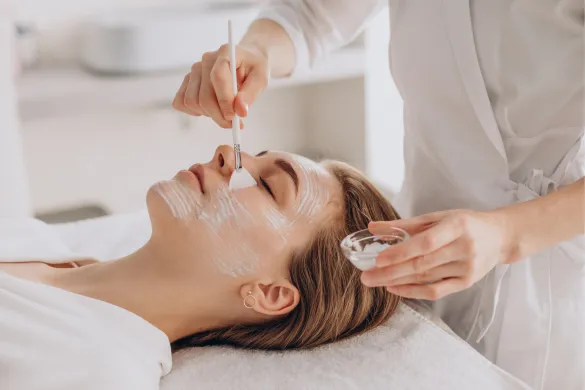 Aesthetician applying a facial mask to a client with a brush.