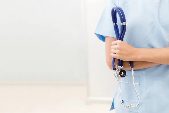 A healthcare professional wearing light blue scrubs and holding a blue stethoscope.