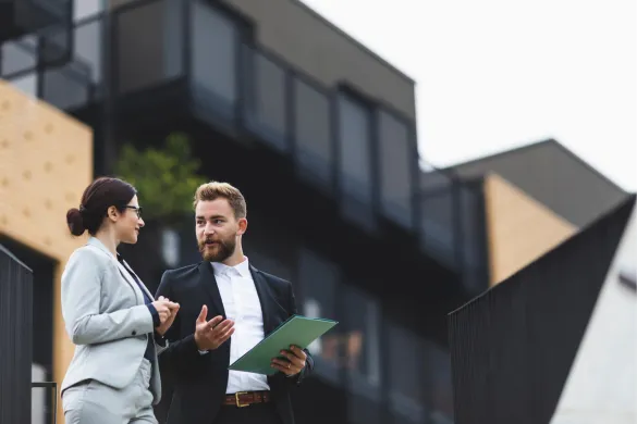 Two business professionals in formal attire talking outside an office building.