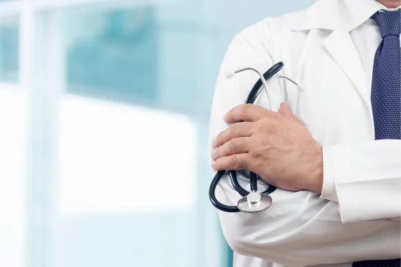 A doctor in a white coat holding a stethoscope with arms crossed.