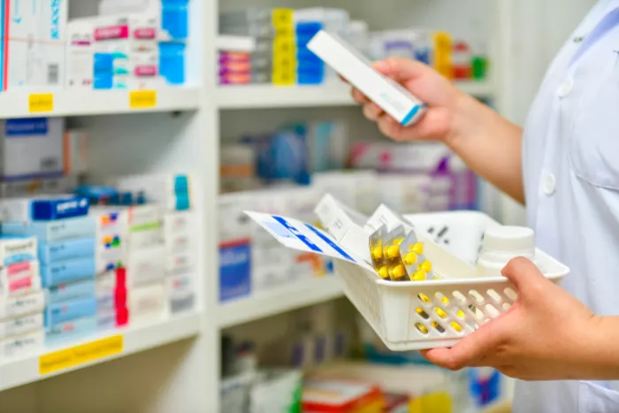 A pharmacist holding a basket of medications while organizing shelves.