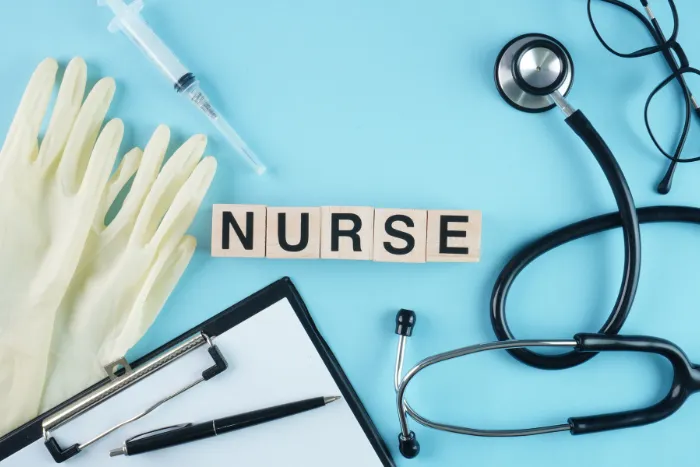 Medical supplies including a stethoscope, clipboard, syringe, and gloves surrounding wooden blocks spelling "NURSE".