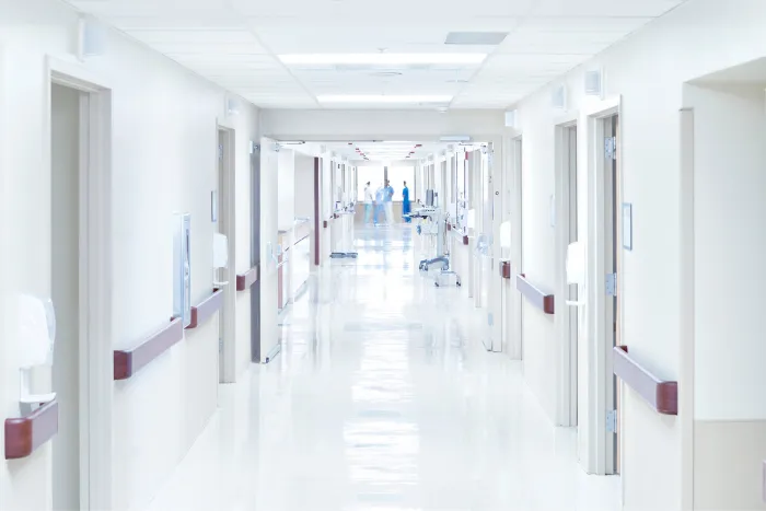 A bright, empty hospital hallway with doors and handrails.