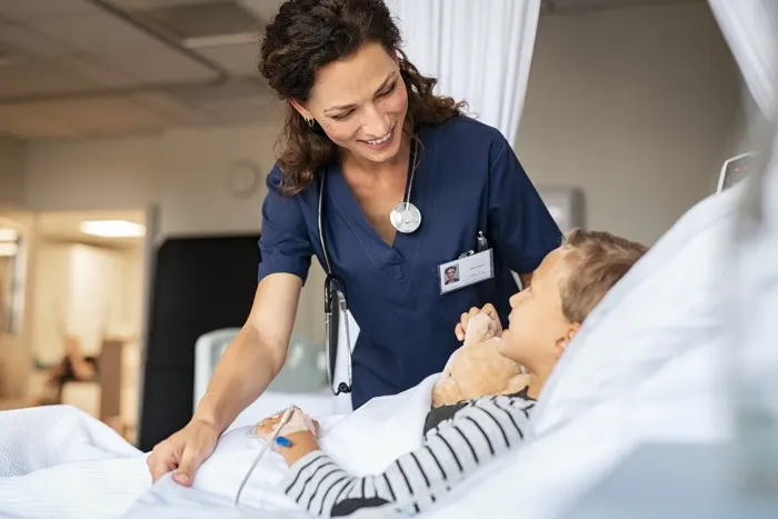 A smiling nurse tending to a young patient in a hospital bed.