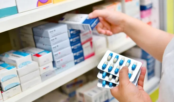 A pharmacist holding blister packs of medication while restocking shelves.