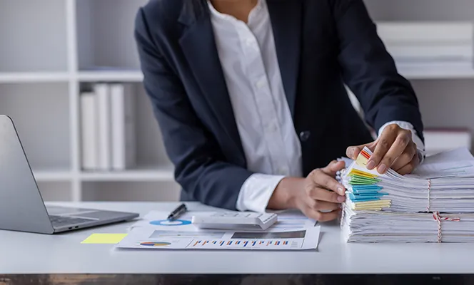 A professional organizing and sorting through a large stack of documents with colorful sticky notes at a desk.