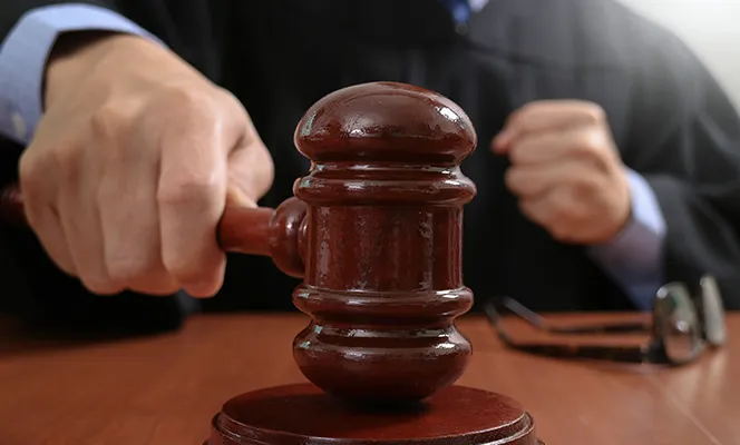 A judge holding a wooden gavel over a sound block in a courtroom.