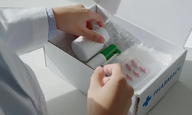 A person packing prescription medications and medical supplies into a pharmacy delivery box