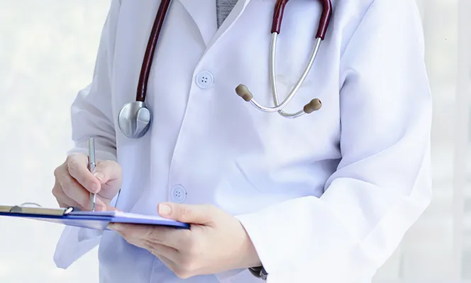 A doctor wearing a white coat and stethoscope while writing on a clipboard.