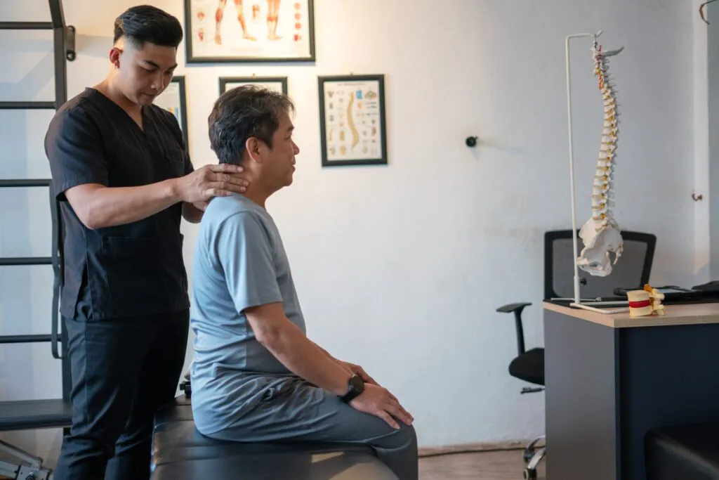 A physical therapist or chiropractor examining a patient's neck in an office with a spine model.