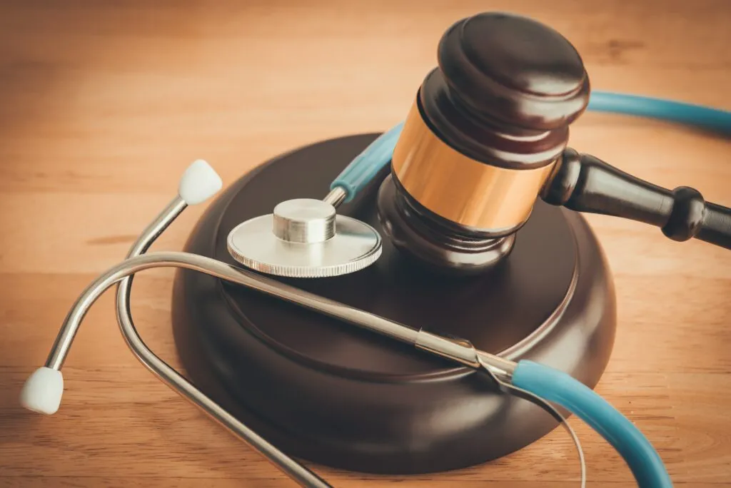 A wooden judge's gavel resting on a sounding block alongside a blue stethoscope on a wooden table.