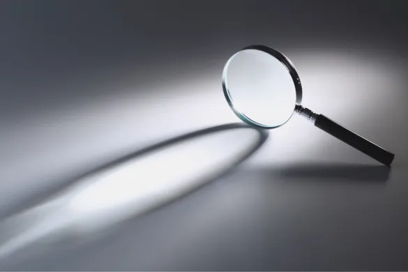 A magnifying glass resting on a surface, casting a bright beam of light and a distinct shadow