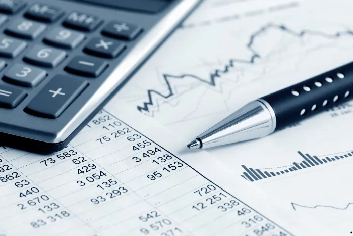 A calculator and a pen resting on financial documents, charts, and data tables.